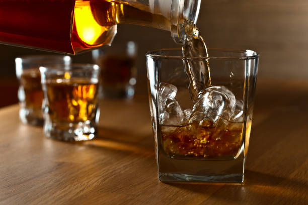 liquor barn forbes: bourbon being poured into a glass with ice cubes