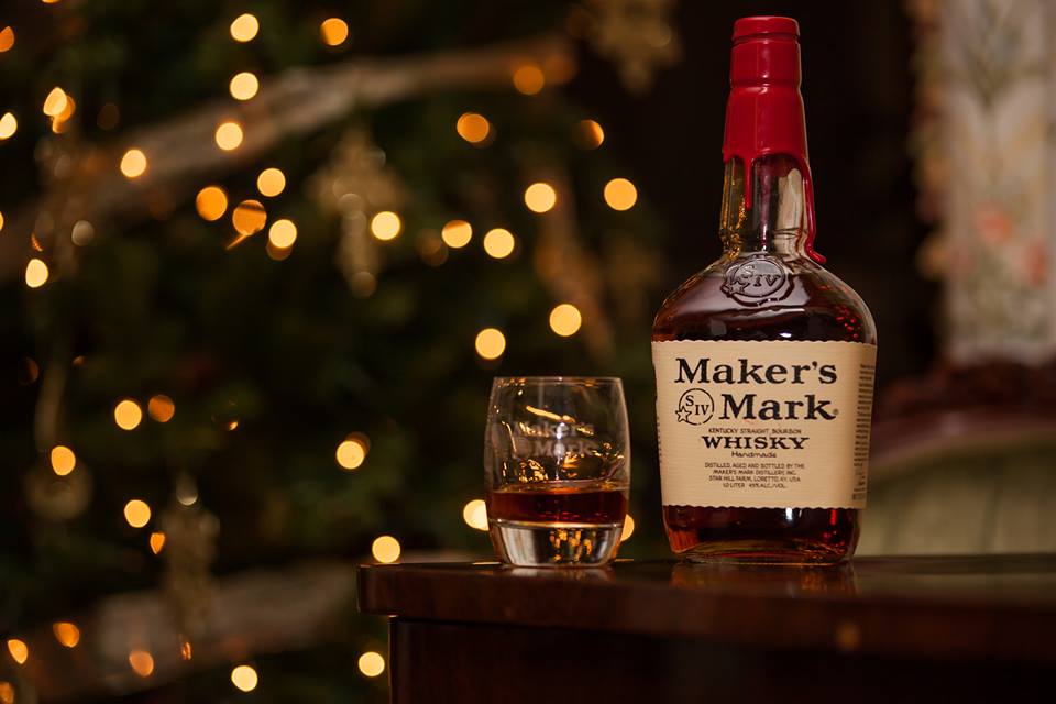 Maker's Mark bottle with glass of bourbon and blurry christmas lights in the background