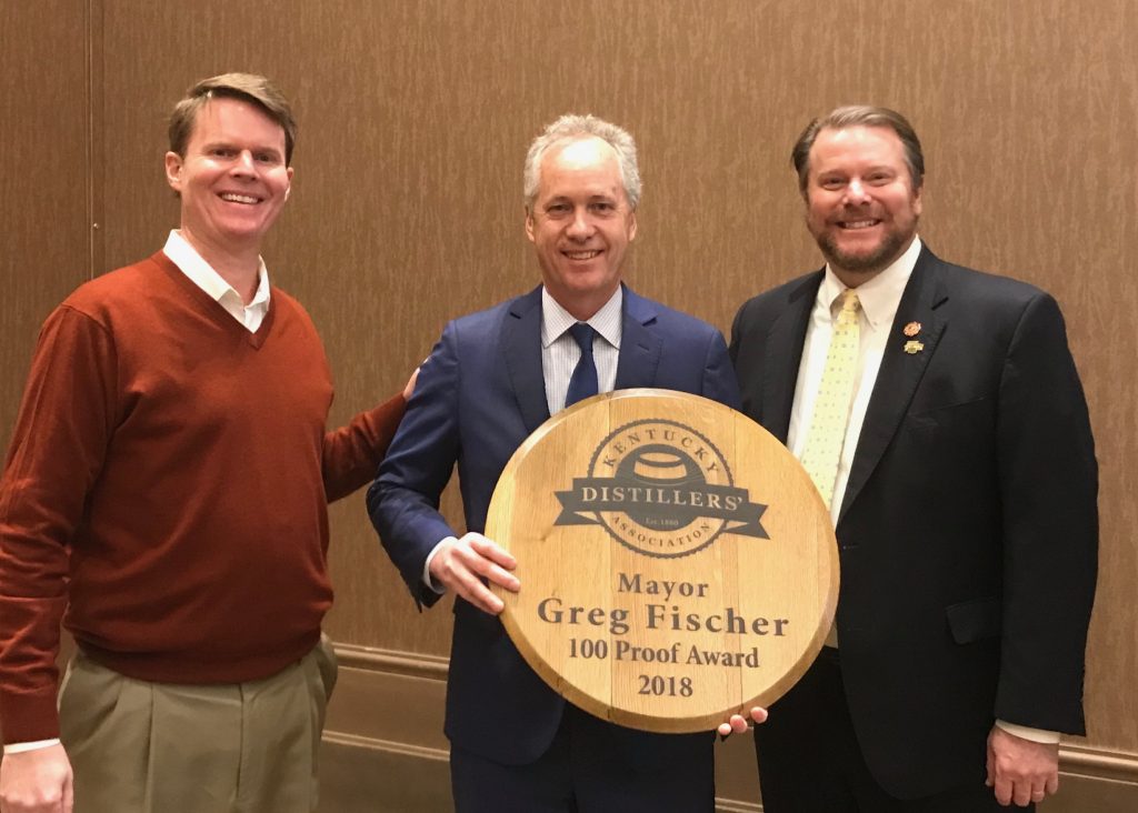 honored: mayor greg fischer holding a barrel head that says 100 proof award with 2 members of the KDA