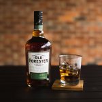 new old forester rye bourbon with a glass of bourbon on the rocks and a blurry brick background