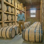kentucky peerless: man in a blue button up and khaki pants standing between bourbon barrels