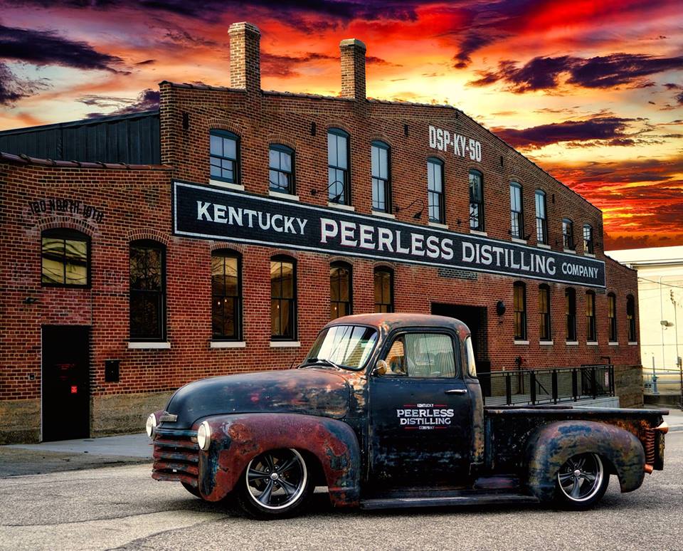 a brick building and an old fashioned truck with kentucky peerless on it and a blazing sun setting