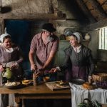 Beers: a man in modern clothing working with ingredients with two women in historic clothing
