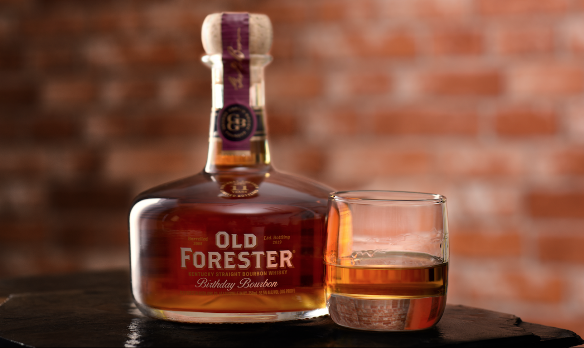 Old Forester: bottle of bourbon and a glass with bourbon and a brick wall in the background
