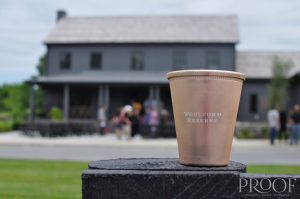 a rose gold cup that says Woodford Reserve and a blurry building in the background