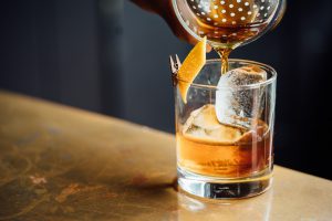 National Bourbon Day: a shaker pouring bourbon in a glass with ice and an orange twist